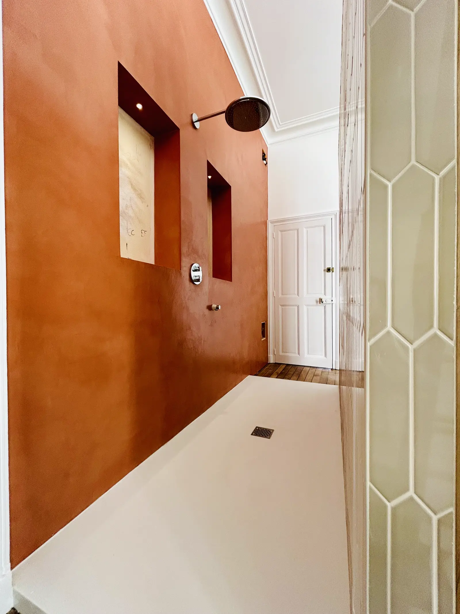 Douche en enduit à la chaux terracotta, vue vers l'entrée de la pièce