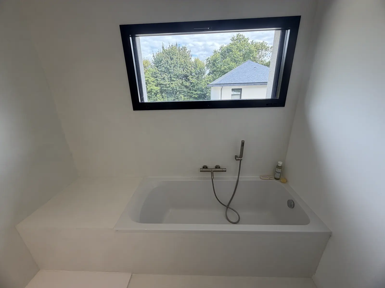 Baignoire en béton ciré sous une fenêtre avec vue sur les arbres