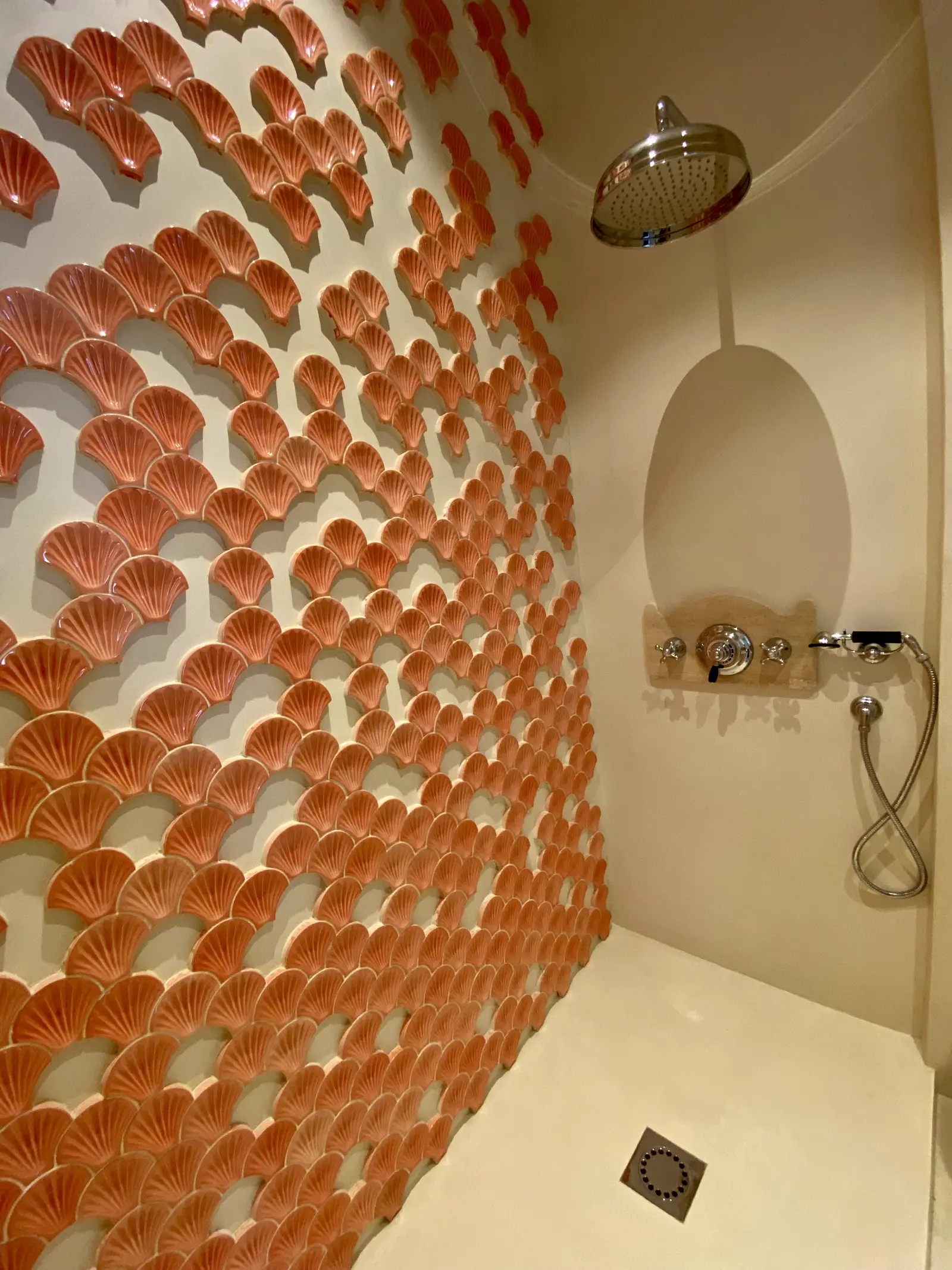 Douche en béton ciré avec mur en céramique motif coquillages orange et robinetterie dorée