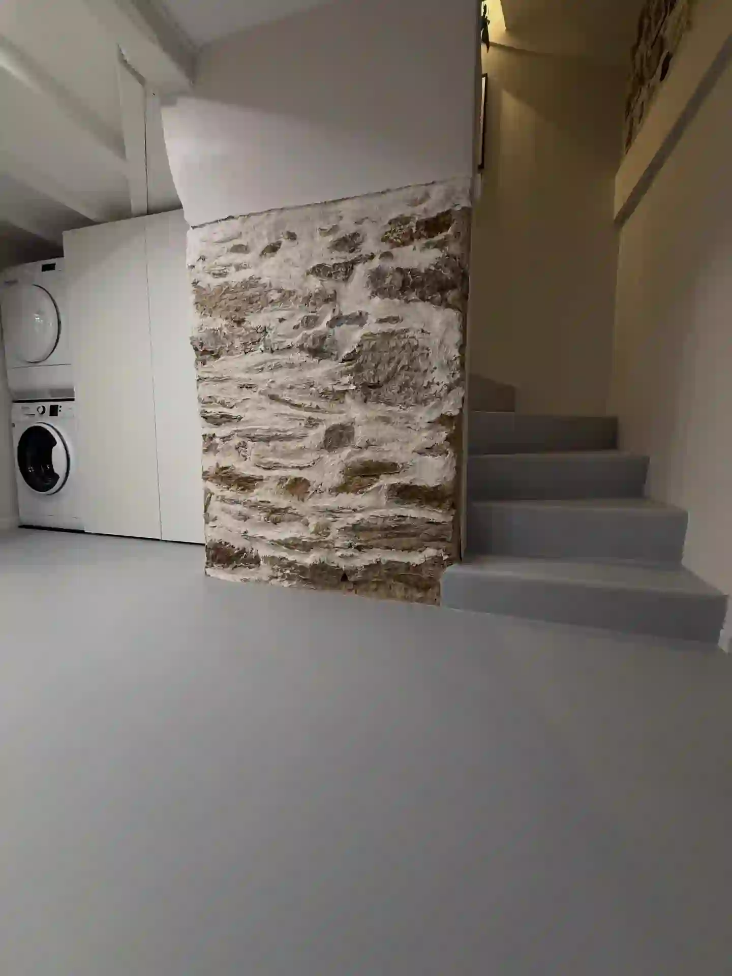 Buanderie avec sol en béton ciré, escalier et mur en pierre