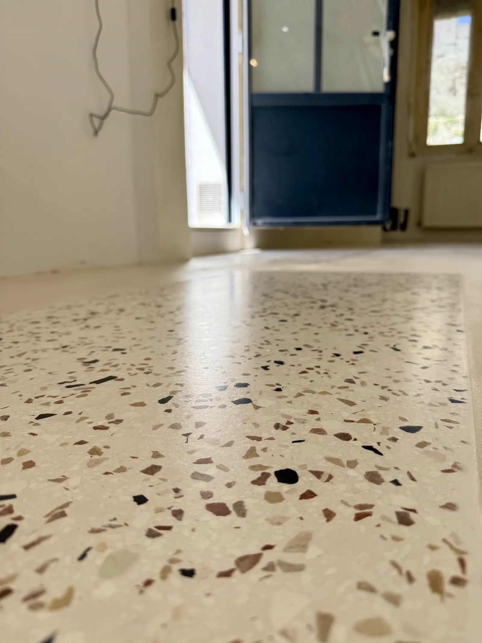 Gros plan sur un sol en terrazzo clair, entrée d'un appartement